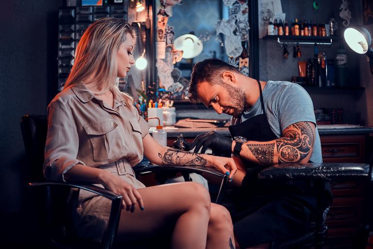 Ein fleißiger Tätowierer kreiert ein neues Tattoo auf der Hand einer jungen Frau im Tatoo-Studio.