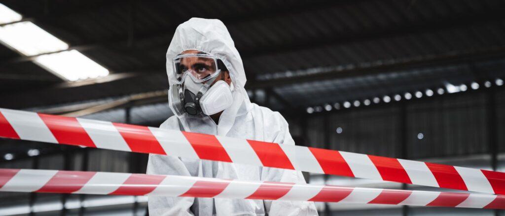 Arbeiter tragen einen Schutzanzug, um chemikalienverunreinigtes Öl in der alten Fabrik zu überprüfen. Rote und weiße Linien markieren eine Gefahrenzone. Kontrolle der Kontamination durch biologische Gefahren