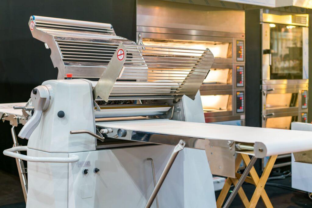 Moderne Teigausrollmaschine in einer Bäckerei mit Edelstahlwalzen.