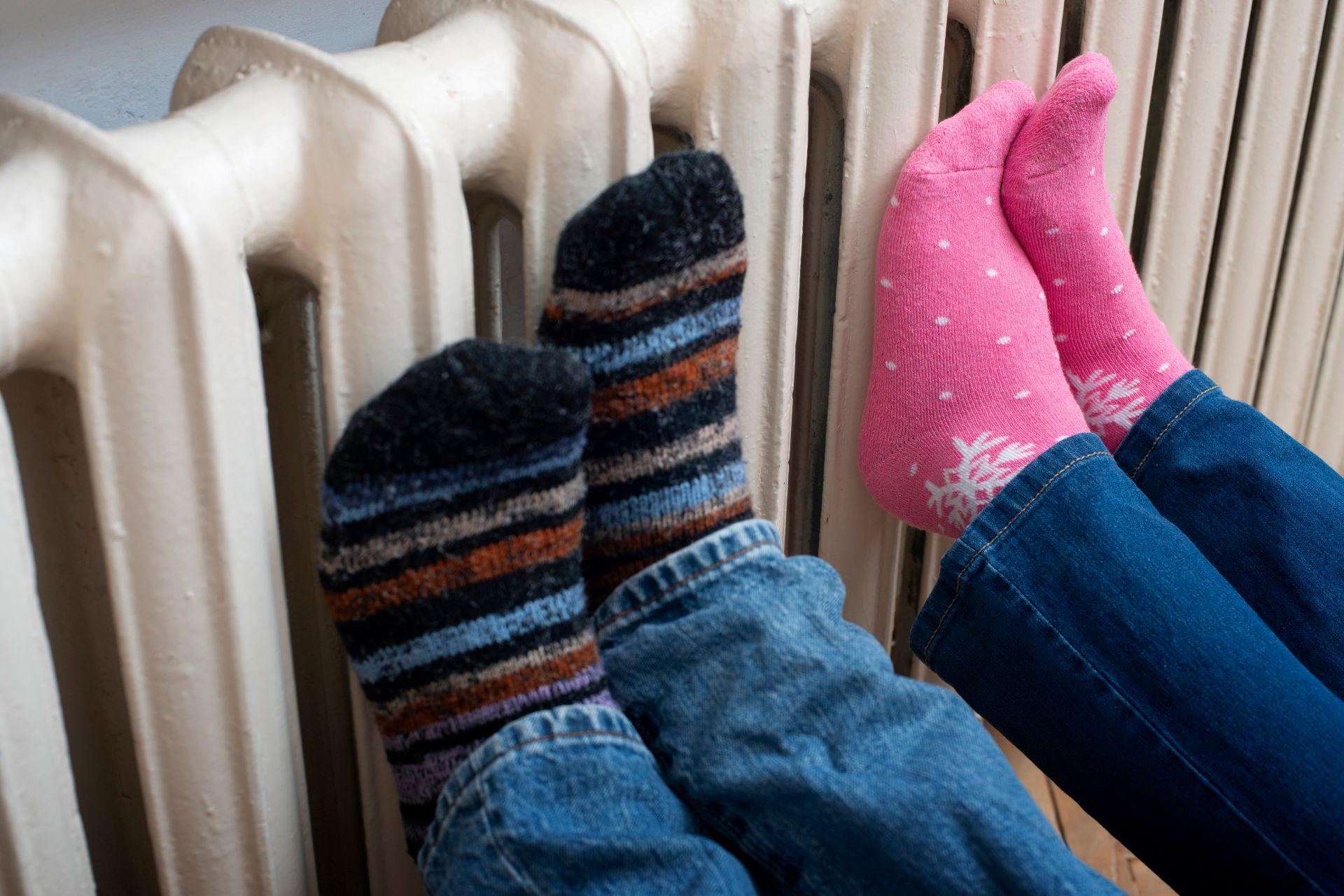 Zwei Personen wärmen ihre Füße an einem Heizkörper – familiäre Winterstimmung passend zum Thema heizölpreise sachsen