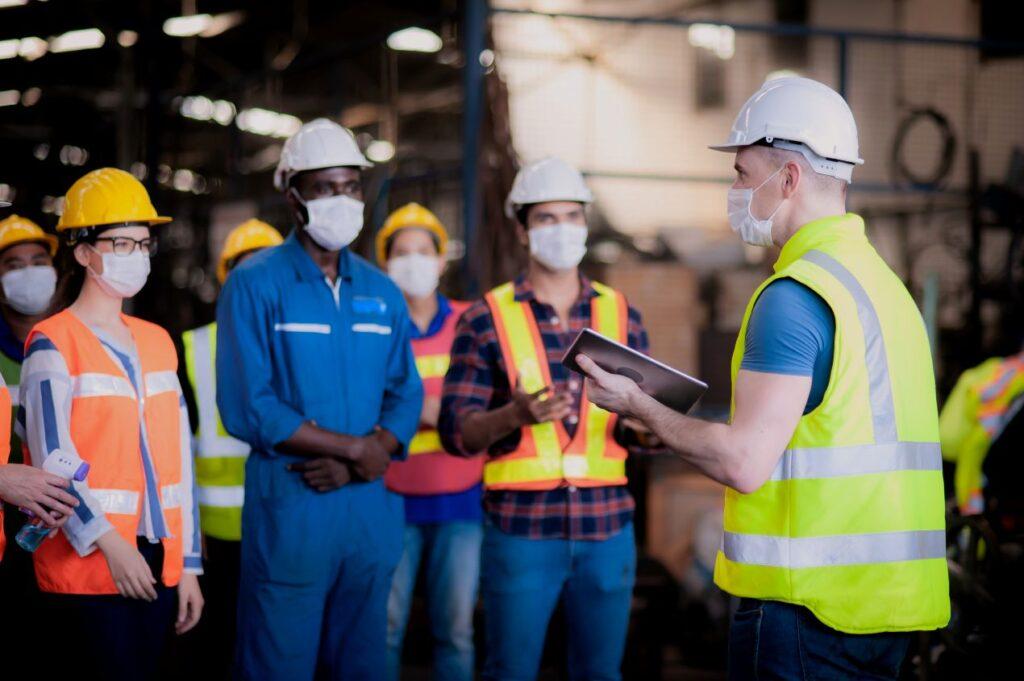 Gruppe von Industriearbeitern mit Masken und Schutzkleidung bei Besprechung zur Reinraumreinigung